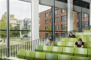 Drei Studierende sitzen in einem grün bestuhlten Hörsaal.
